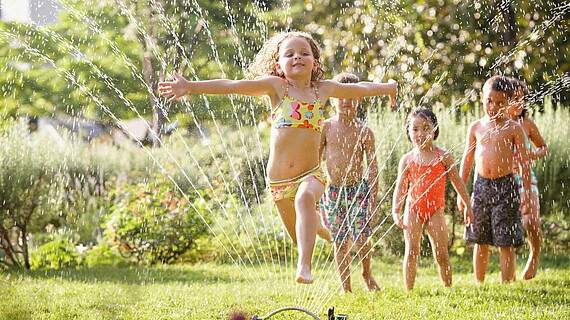 Kinder spielen mit einem Wasserschlauch im Garten